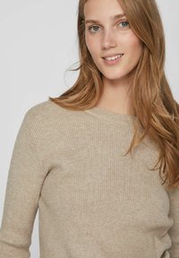 Pulover bej cu dungi, cu gât rotund și mâneci lungi, având o textură moale și detalii de design minimale, pe un fundal neutru.