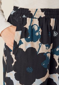 Blomstrede bukser i let stof med sort bund og store blå og beige blomster, elastisk talje og sidelommer.