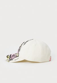 Casquette de baseball blanche avec une visière courbée, ornée d'un motif graphique rose et noir sur la visière et d'une étiquette de marque sur le côté.