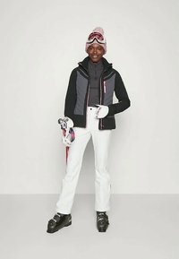 Ski riided, mis koosnevad mustast ja hallist jakkist roosa aktsendiga, valgetest püksidest, mustadest suusasaabastest ja suusagloobidest koos roosa pom-pom mütsiga.