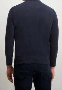 Marinblå stickad tröja med rund halsringning, ribbade ärmslut och nederkant. Har en diskret vertikal söm längs axlarna.