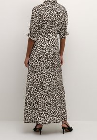 Maxikleid mit Leopardenmuster aus leichtem Stoff, mit kurzen Ärmeln, einem Kragen und einem taillierten Gürtel. Schwarze Absatzschuhe runden den Look ab.
