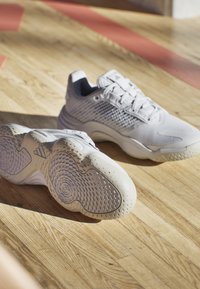 Baskets de sport gris clair avec une tige en mesh texturé, un col rembourré et une semelle en caoutchouc présentant des motifs circulaires et un design de traction unique.