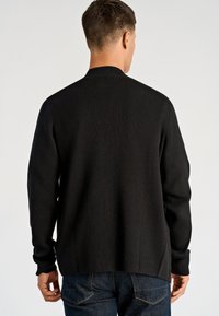 Czarny prążkowany sweter z wysokim kołnierzem, długimi rękawami i bocznymi rozcięciami u dołu. Faktura tkaniny tworzy subtelny, strukturalny wygląd.