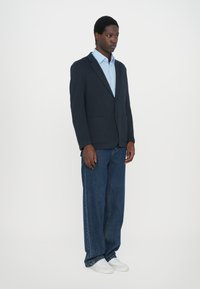 Blazer navy con dos bolsillos frontales, camisa celeste debajo, combinado con jeans azules de corte holgado y zapatillas blancas.