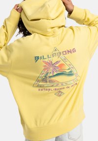 Yellow hooded sweatshirt featuring a colorful graphic of palm trees and mountains in a triangular design on the back. Soft, cotton material.