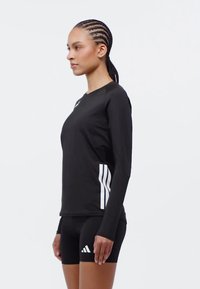 Černé dlouhé sportovní tričko s bílými bočními pruhy, spárované s černými šortkami s malým bílým logem Adidas na levém stehně.
