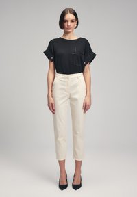 Black short-sleeve top with a front pocket, paired with cream tapered trousers and black pointed heels. Smooth textures, simple design.
