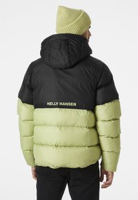 Chaqueta tipo plumón con parte superior negra y sección inferior verde claro, que presenta secciones acolchadas horizontales y capucha. Incluye la marca "HELly HANSEN".
