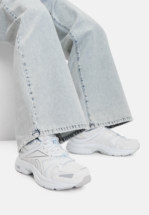 Sneaker atletici bianchi con pannelli in rete e dettagli testurizzati. Abbinati a jeans in denim a gamba larga di colore azzurro chiaro con orli sfrangiati.