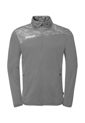 Grijze sportjas met rits en een geometrisch patroon op de schouders, met het "Kempa"-logo op de linkerbovenkant van de borst, voorzien van twee met rits afsluitbare zijzakken.