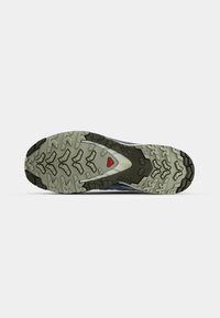 Trail shoe outsole featuring a rugged design, black rubber with deep treads, and a grey midsole with a red accent near the heel.