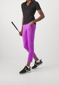 Person in black polo and bright purple checkered pants holding a golf club, wearing black Nike sneakers and white socks.