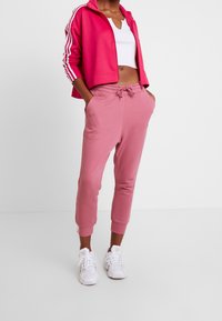 Dopasowane różowe dresy z bocznymi kieszeniami i ściągaczami, w połączeniu z krótko skrojoną jasnoróżową bluzą z zamkiem, ozdobioną białymi paskami. Białe sneakersy.