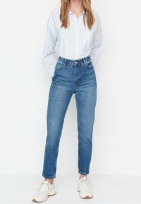 Blue high-waisted denim jeans with a straight leg cut. Paired with a light blue striped button-up shirt and white sneakers.