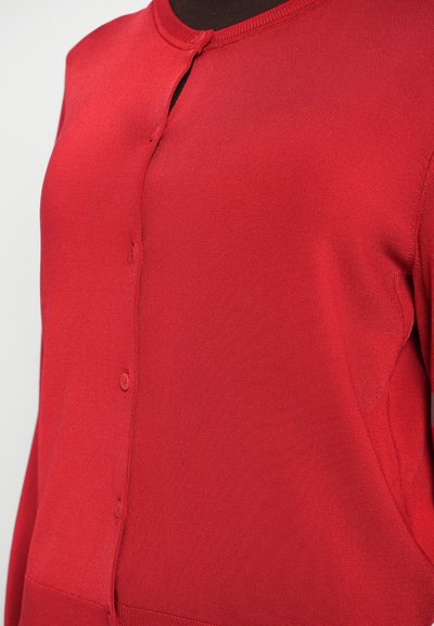 Czerwona bluzka zapinana na guziki, wykonana z prążkowanej dzianiny, z okrągłym dekoltem i dwoma widocznymi guzikami na środku przodu.
