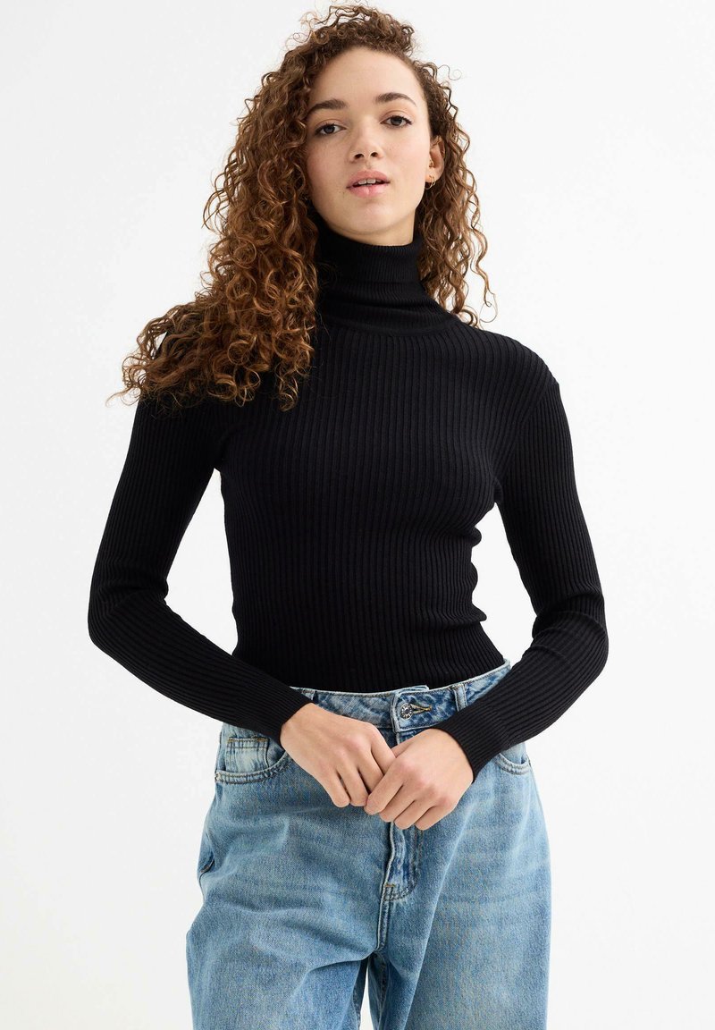 Top negro de cuello alto con canalé y mangas largas, combinado con unos vaqueros de denim de tiro alto en azul claro, con un ajuste relajado y detalles de costura visibles.