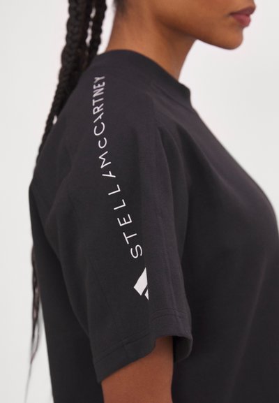 T-shirt noir avec un col rond, présentant une coupe ample et des manches courtes. La manche affiche des lettres blanches "STELLA McCARTNEY" et un accent logo.