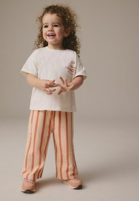 Camiseta blanca de manga corta con estampado rojo de "Disney PRINCESS", combinada con pantalones anchos a rayas melocotón y crema y zapatillas ligeras.