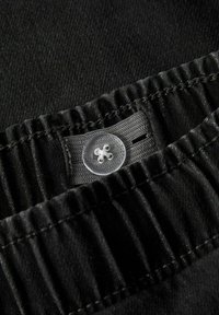 Cinturilla de tela negra con textura fruncida, que presenta un botón transparente con un patrón intrincado, cosido de forma segura a la cinturilla.