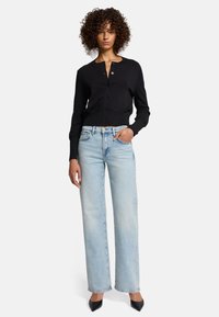 Cardigan nero lavorato a maglia con bottoni, abbinato a jeans dritti a vita alta di color blu chiaro e tacchi a punta neri.