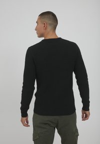 Schwarzer Strickpullover mit strukturiertem Design an der oberen Rückseite und an den Ärmeln. Runder Ausschnitt und enganliegende gerippte Bündchen und Saum.