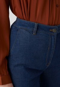 Jeans in denim blu scuro con vita alta, dotati di chiusura con bottone, tasche laterali e dettagli di cucitura a contrasto.