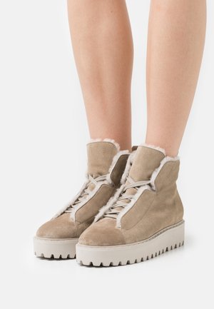 Bottines en suède beige avec une bordure en fourrure douce, bout rond et semelle en caoutchouc blanc épais présentant un motif texturé en zigzag.