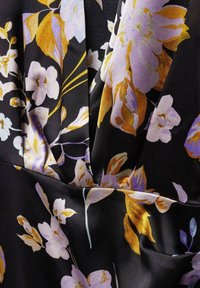 Tissu noir à grand motif floral avec des fleurs violettes et dorées. Texture lisse avec plis et éclat subtil.
