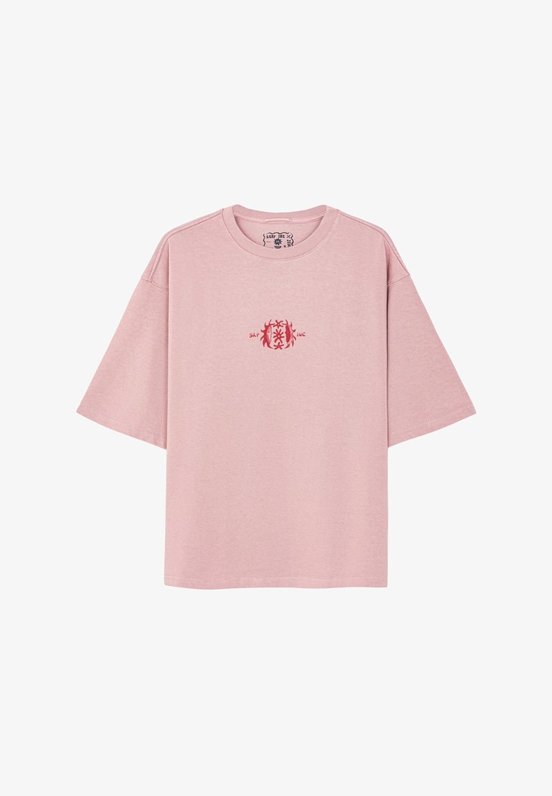 Różowa bawełniana koszulka z luźnym krojem, krótkimi rękawami, okrągłym dekoltem i małym czerwonym wzorem na piersi.