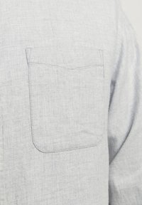 Heledhall hallide särk, millel on tekstuuriga kangas ja üks rinna tasku, millel on peen õmblustega kujundus. Nähtavaid nuppe ega kaunistusi ei ole.