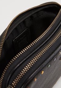 Portafoglio in pelle nera con superficie testurizzata, cerniera color oro e borchie arcobaleno lungo il davanti per un dettaglio in più.