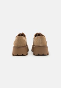 Brown suede shoes with a thick platform sole, featuring a textured finish and a rounded toe. The design includes seaming details.