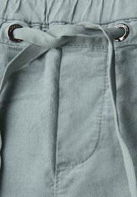 Tissu en velours côtelé bleu clair au toucher lisse, avec un cordon réglable doté d'un œillet métallique et des détails de poche cousus.