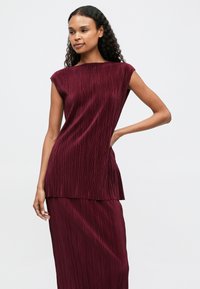 Μπορντό πλισέ φόρεμα με φάσα και καπ σλίβες, με χαρακτηριστικά στρωτή σχεδίαση και μαλακό, υφασματοποιημένο ύφασμα.