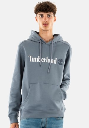 Grijze hoodie met een voorzak, trekkoorden en een wit "Timberland" logo. Zacht materiaal, ribbelboorden en -onderkant, minimalistisch design.