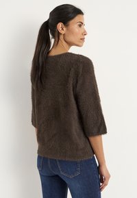 Bruine fuzzy trui met driekwartmouwen, ronde halslijn en een relaxte pasvorm, gecombineerd met donkerblauwe, aangesloten jeans.