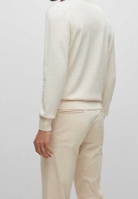 Beige stickad tröja med rund halsringning, ribbade muddar och fåll. Matchad med ljusbeige byxor med en bakficka och slät textur.