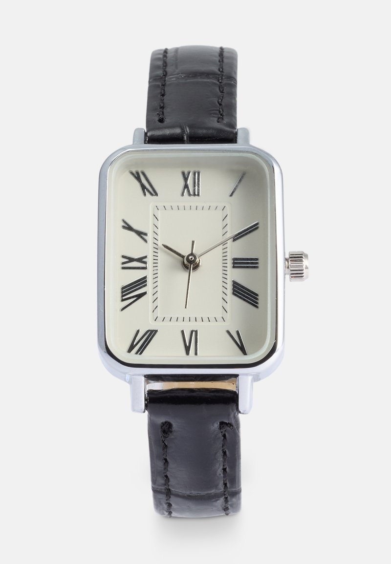 Reloj rectangular plateado con una esfera color crema, números romanos negros y una correa de cuero negro con un sutil detalle de costura.