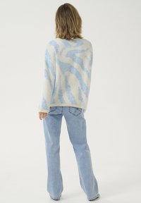 Overmaatse crème en lichtblauwe trui met golvende patronen, gecombineerd met lichtblauwe flared jeans met achterzakken en stiksels.