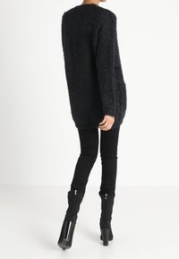 Czarny, długi, puszysty sweter z luźnym krojem, połączony z dopasowanymi czarnymi spodniami i czarnymi botkami na obcasie z zamkiem błyskawicznym.