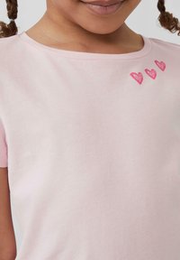 Helles rosa Baumwoll-T-Shirt mit kurzen Ärmeln und rundem Ausschnitt, verziert mit drei gestickten pinken Herzen auf der Brust.