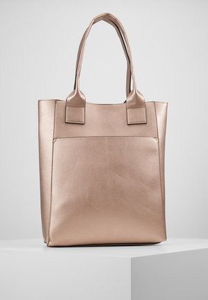 Beige Leder-Tragetasche mit zwei Griffen, rechteckiger Form und großer Außentasche, auf einem weißen Podest vor grauem Hintergrund präsentiert.
