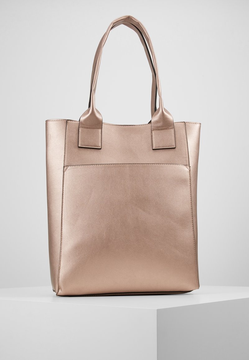 Sac fourre-tout en cuir beige avec deux poignées, de forme rectangulaire et une grande poche extérieure, présenté sur un socle blanc sur un fond gris.