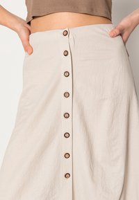 Falda midi de color beige claro hecha de un tejido texturizado, con botones marrones en la parte delantera y bolsillos laterales.