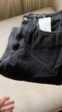 Černé džínové kalhoty s jemnou texturou, s tkanicí v pase a připojenou štítkem na oblečení. Tkanina má mírný lesk.