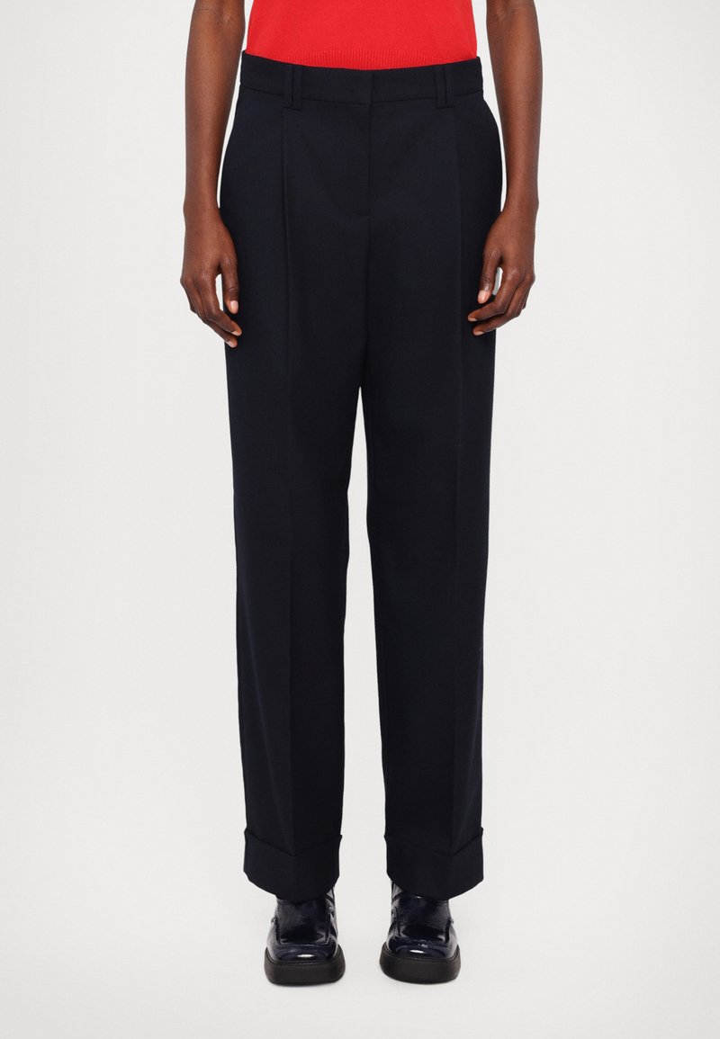 Pantaloni sartoriali blu scuro con davanti piatto, pieghe e fondo con risvolto. Realizzati in un tessuto liscio, presentano passanti per cintura e tasche laterali.