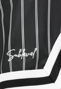 Schwarz-weiß gestreutes Gewebe mit strukturierter Oberfläche. Auffälliges gesticktes "Sublevel"-Logo nahe dem Boden und kontrastierende weiße Akzente.