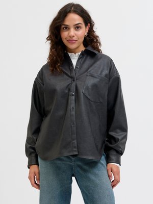 Zwarte faux leren shirt met een kraag, voorzak en knoopsluiting. Lange mouwen, relaxed fit en een gladde textuur.