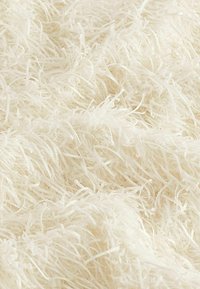 Un textile blanc et duveteux présentant de longues fibres douces et bouclées avec une texture brillante, créant un effet de superposition.